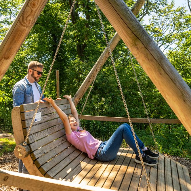Große Holzschaukel mit Liegefläche, auf der eine Frau liegt